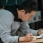 Repair shop owner writing customer and inventory records by hand on paper before switching to repair shop software